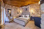 Cozy bedroom with stone walls, wooden ceiling, and a bed with white bedding.