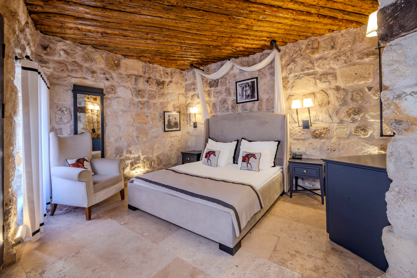 Cozy bedroom with stone walls, wooden ceiling, and a bed with white bedding.