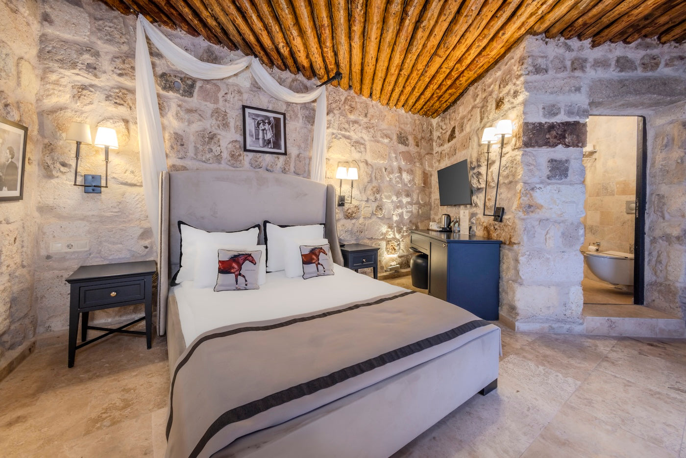 Bedroom with stone walls and wooden ceiling, featuring a bed with white bedding and decorative pillows.